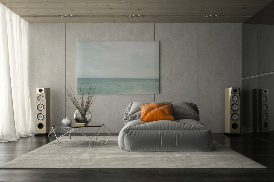 A modern living room featuring a gray couch, a painting, and stylish speakers.