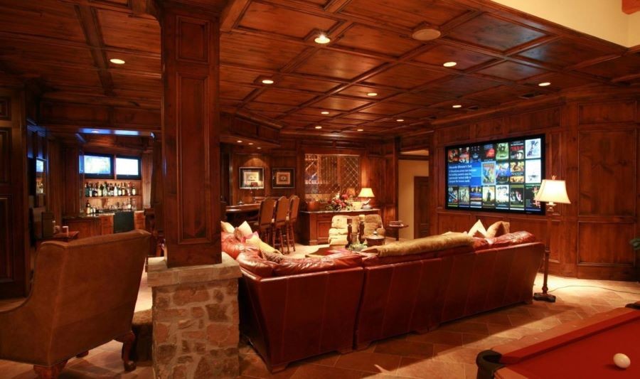 A home entertainment room with a large display, in-ceiling speakers, pool table, and bar with two TVs.